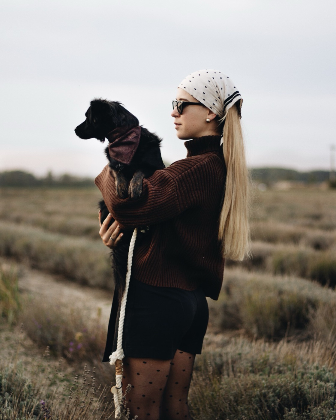 Woman in a brown sweater holding a black dog in a lavender field